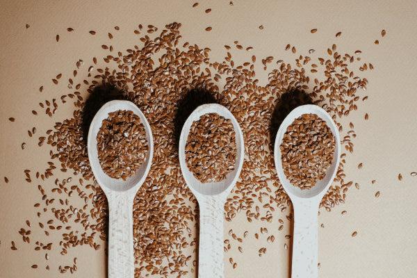 Three spoons half filled with flax seeds on a surface covered in flax seeds