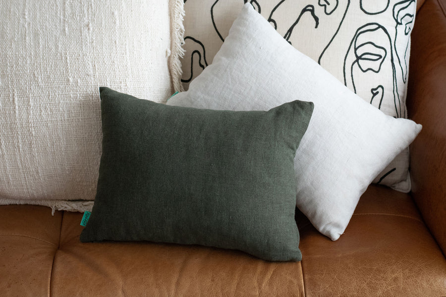 Two Kind Face Linen Travel Pillows in Moss and Oyster on a Leather Couch 